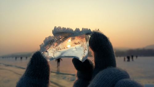 Cropped hand holding ice during sunset