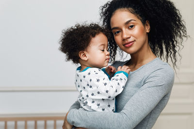 Portrait of confident smiling mother carrying baby boy at home