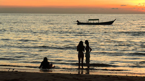 People in sea against sky during sunset