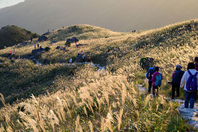 Rear view of people walking on field against mountain