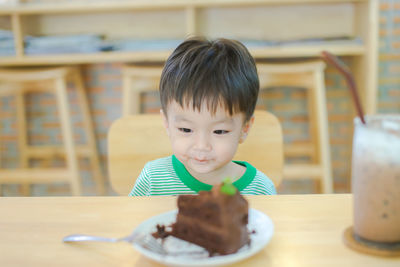 Cute boy with slice of cake in plate on table