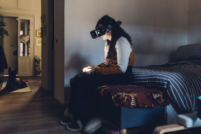 Woman sitting on bed using virtual reality headset at home