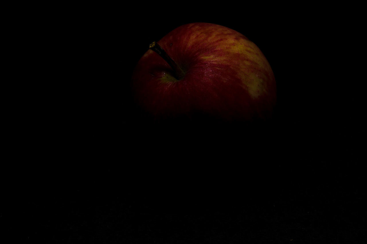 CLOSE-UP OF APPLE ON BLACK BACKGROUND AGAINST ORANGE