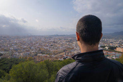 Rear view of man looking at city buildings against sky