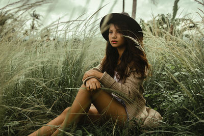 Thoughtful woman sitting on grassy field at forest