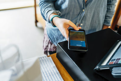 Midsection of female customer making mobile payment at store