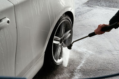 Cropped unrecognizable man with hose washing car at washing station