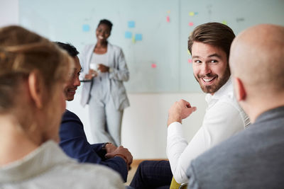 Smiling businessman looking at male colleague during presentation while sitting in office seminar