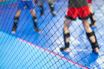 Low section of men practicing martial arts seen through chainlink fence