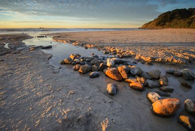 Rocks on beach against sky during sunset