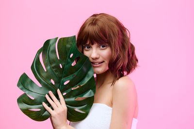 Portrait of young woman standing against pink background