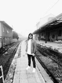 Full length portrait of young woman standing on road against sky