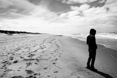 Rear view of woman walking on beach against sky