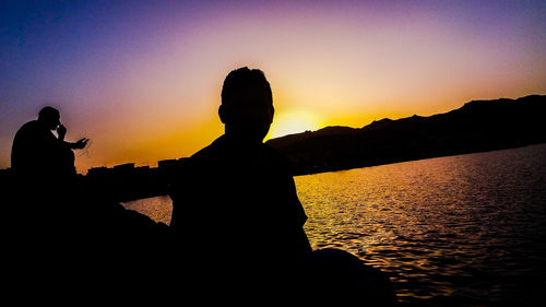 Silhouette people standing by sea against orange sky