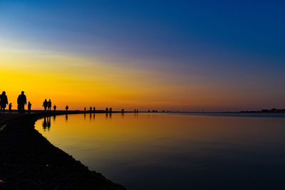 Silhouette people at beach against sky during sunset