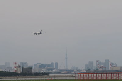 Airplane flying over buildings in city against sky