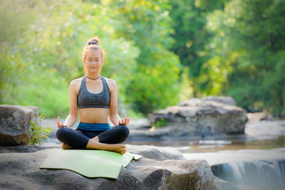 Teenage girl meditating while sitting on rock against trees in forest