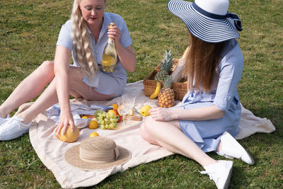 A two young women in a similar blue dress is resting on a picnic, chees plate