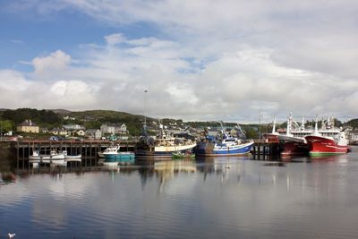 Boats moored in harbor against cloudy sky