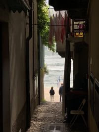 Rear view of people walking on alley amidst buildings in city