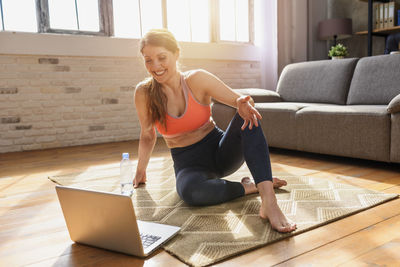 Full length of happy young woman using laptop at home