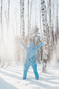 Rear view of man wearing costume standing against trees on snowy field in winter