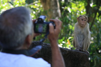 Man holding camera while sitting by tree