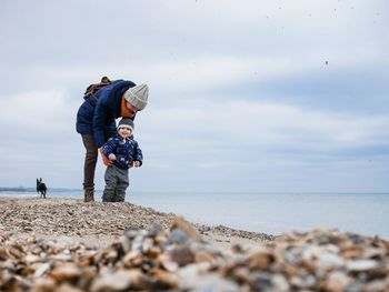 Father and son standing at beach against sky