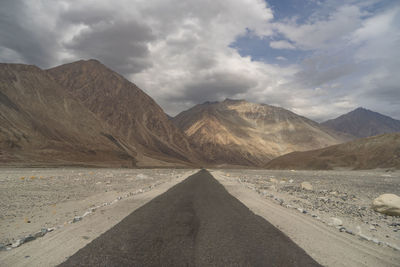 Road leading towards mountains against sky