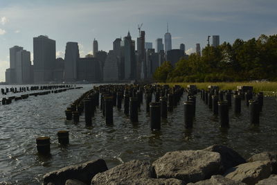 Wooden posts in river by buildings against sky