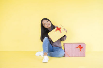 Portrait of beautiful young woman sitting against yellow wall