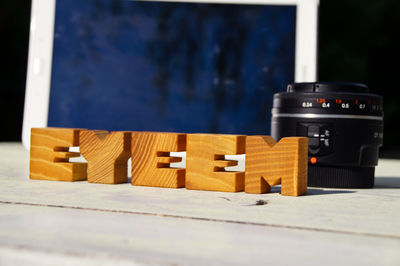 Close-up of wooden eyeem text by camera lens on table