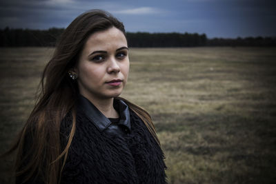 Portrait of young woman standing on field against sky