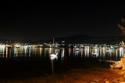 Illuminated buildings by lake against sky at night