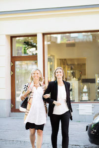 Happy female friends walking with arm in arm on city street