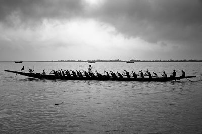 Silhouette people on boat in river against sky