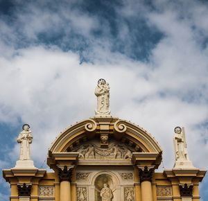 Low angle view of sculptures on historic building against cloudy sky