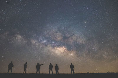 Low angle view of silhouette people standing on field against star field at night