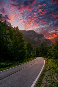 Road by trees against sky during sunset