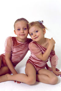 Two sisters girl sitting on a white background in pink bodysuits