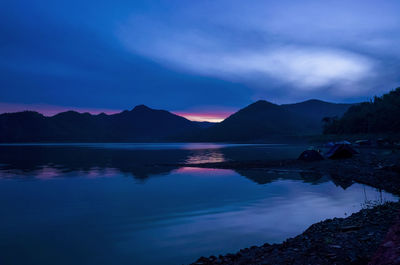 Scenic view of lake by silhouette mountains against sky at sunset