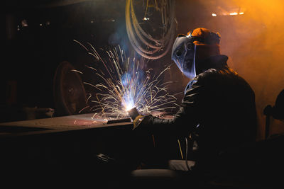 Persona working with an electric welding machine. a man in safety glasses and a leather jacket cooks