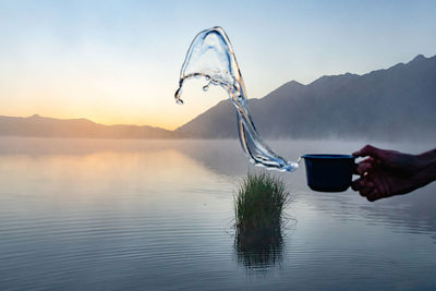 Cropped hand throwing water in lake against sky