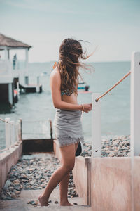 Rear view of woman standing by sea against sky