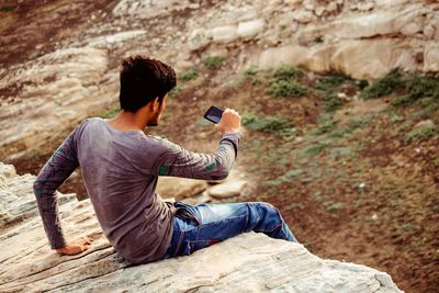 Man photographing while sitting on rock