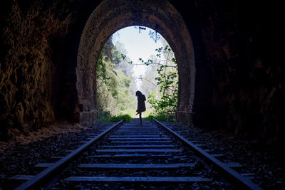 Rear view of woman standing on railroad track in tunnel