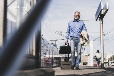 Mature businessman walking at train platform with suitcase and briefcase