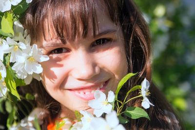 Close-up portrait of cute girl by white flowers blooming outdoors