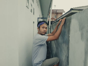 Portrait of young man looking away while standing against wall