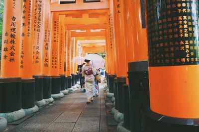Rear view of women walking on walkway amidst torii gates